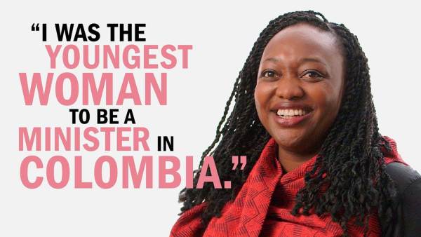 Paula Moreno has black braided hair and is wearing a black dress with a red wrap. She's standing next to copy that reads, "I was the youngest woman to be a minister in Colombia."
