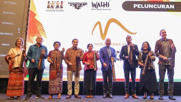 Representatives from the Ford Foundation and Indonesian NGOs smile and hold traditional musical instruments on stage. Behind them is an illuminated screen with the logos of the various organizations.