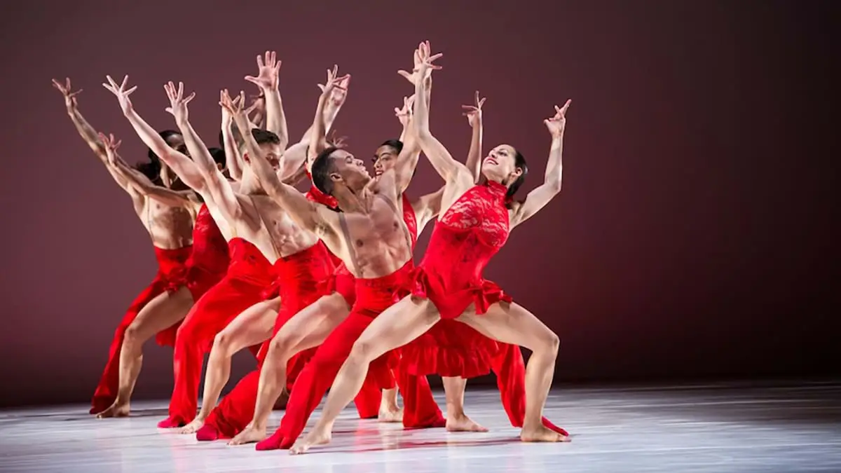 Group of dancers wearing red with their arms raised in the air.